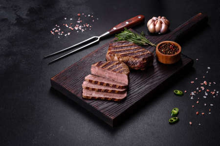 Fresh juicy delicious beef steak on a dark background. Meat dish with spices and herbsの写真素材