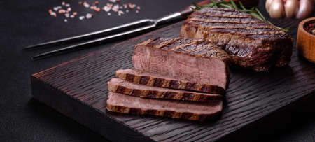 Fresh juicy delicious beef steak on a dark background. Meat dish with spices and herbs