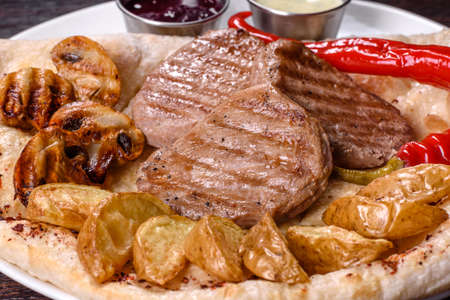 Delicious juicy chicken steak with baked potatoes, mushrooms and sauces on a white dishの写真素材