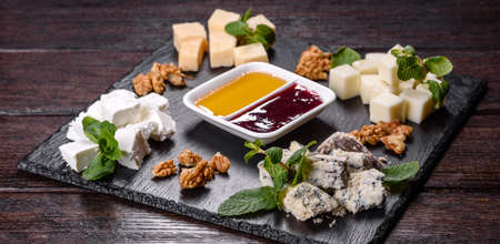 Several types of cheese on a shale tray with mint and sweet sauces. Snacks to the festive tableの写真素材