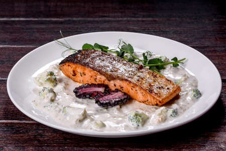 Tasty baked salmon fish on a white dish with broccoli, white sauce and pea sproutsの写真素材