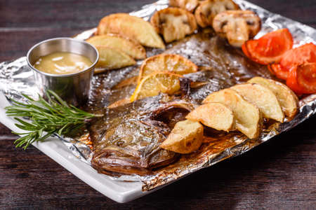 Tasty fried fish with potatoes and tomatoes on a white rectangular dish. Preparation of the festive tableの写真素材