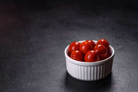 Delicious red canned cherry tomatoes in white piala on a dark concrete tableの写真素材