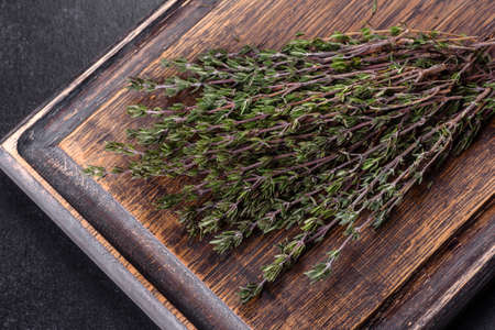 Bundle of fresh thyme grass on a wooden cutting board on a dark concrete table