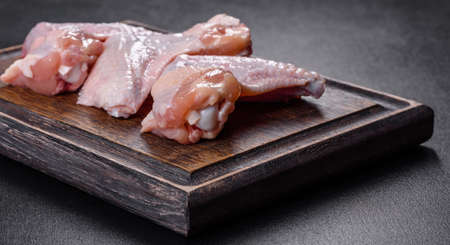 Raw meat. Chicken wings lie on a wooden board with vegetables and spices on a black backgroundの写真素材