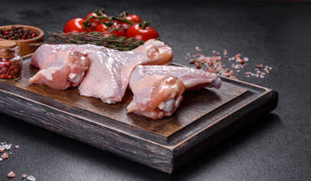 Raw meat. Chicken wings lie on a wooden board with vegetables and spices on a black backgroundの写真素材