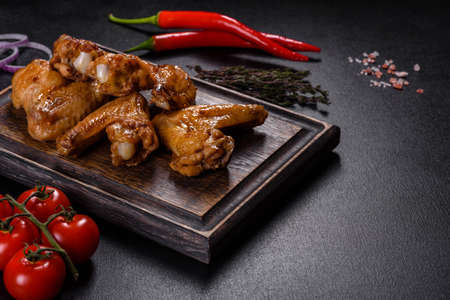 Crispy barbecue chicken wings with vegetables and spices on a black backgroundの写真素材