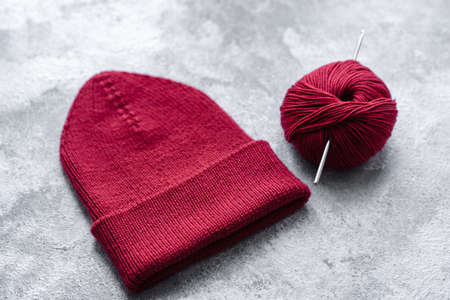 Red warm knitted women's hat on a concrete background. Hobbies and leisure time