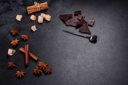Broken black chocolate pieces with star anise and cinnamon on black background