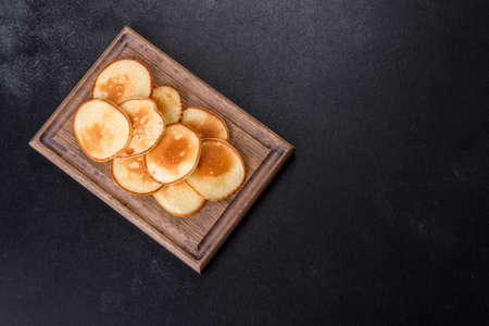 Delicious fresh pancakes on a wooden cutting board with sugar on a dark concrete backgroundの写真素材