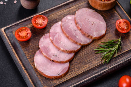 Delicious fresh ham cut with slices on a wooden cutting board on a dark concrete background