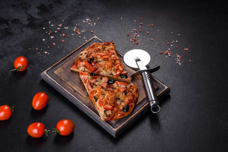 Small homemade vegetable pizza with addition of tomatoes, olives and herbs on a dark conkrete table