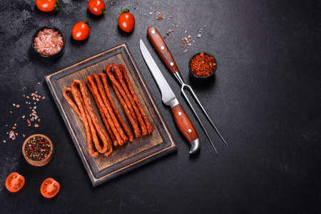 Delicious fresh bright smoked hot sausages with cherry tomatoes on a dark concrete tableの写真素材