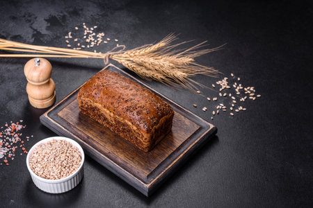 Fresh baked brown bread with ears and grains of wheat on a dark concrete background