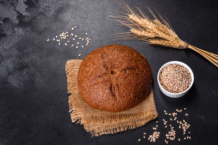 Fresh baked brown bread with ears and grains of wheat on a dark concrete background