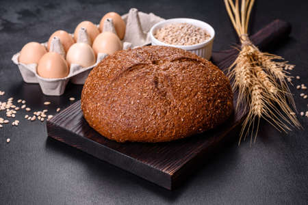 Fresh baked brown bread with ears and grains of wheat on a dark concrete backgroundの写真素材