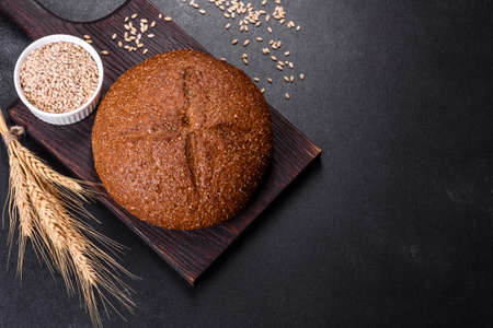 Fresh baked brown bread with ears and grains of wheat on a dark concrete backgroundの写真素材