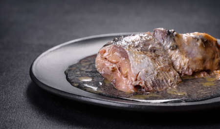 Canned sardine in oil on a black round plate against a dark concrete background. Making a delicious...