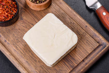 Block of mozzarella cheese and pieces on wooden cutting board