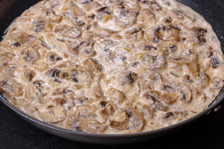 Delicious fresh young champignons sliced into slices in creamy sauce simmered in a black panの写真素材