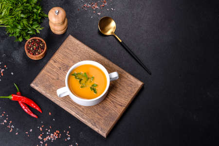 Delicious fresh pumpkin puree soup decorated with parsley in a white plate against a dark concrete backgroundの写真素材