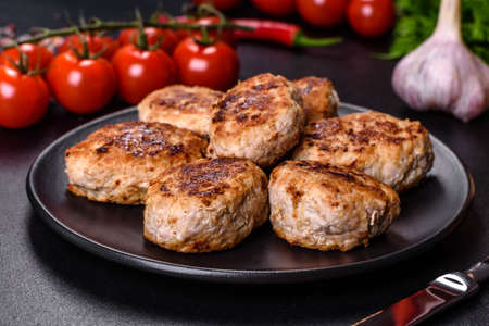Fried cutlets from minced meat in frying pan and spices on a dark concrete background