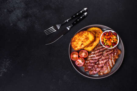 Slices of delicious grilled bacon with croutons fried in egg with spices, salt, vegetables and herbs against a dark concrete backgroundの写真素材