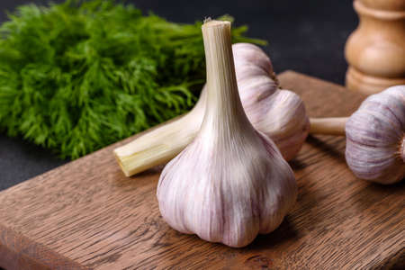 Heads of fresh white garlic on a wooden cutting board against a dark concrete background. Cooking at...