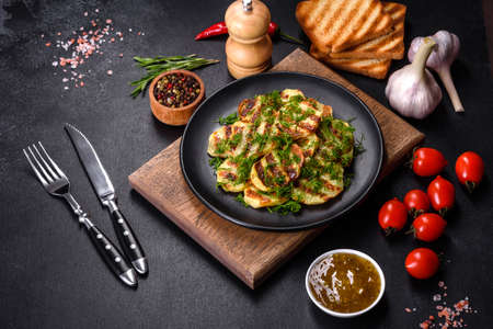 Delicious grilled potato slices with spices and herbs on a black plate against a dark concrete...