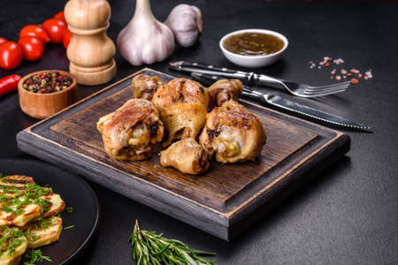 Three chicken legs grilled with spices and herbs on a wooden cutting board against a dark concrete background. Cooking at homeの写真素材