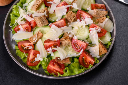 Delicious spring fresh vegetable salad with cherry tomatoes, cucumber, breadcrumbs and parmesan cheese on a dark concrete backgroundの写真素材