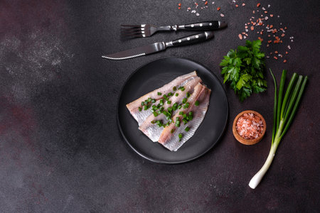 Delicious fresh herring fillet with salt, spices and herbs on a black plate against a dark concrete backgroundの写真素材