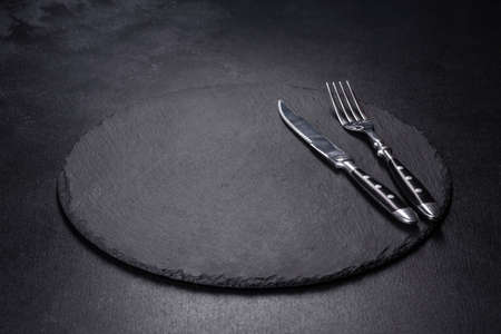 Empty black plates, fork and knife on a black background. Top view, copy space