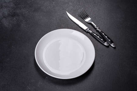 Empty white plates, fork and knife on a black background. Top view, copy spaceの写真素材