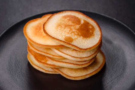 Delicious fresh pancakes on a black plate against a dark concrete background. Making a delicious...