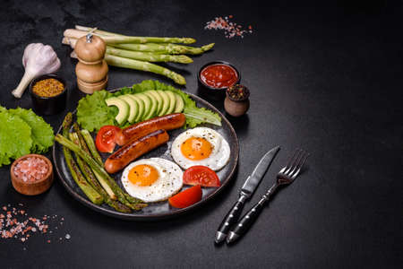 A delicious nourishing breakfast with fried eggs, sausages, asparagus, tomatoes, avocado, spices and...