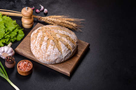 White round bread with flax seeds on a cutting board against a dark concrete background. Baking at...
