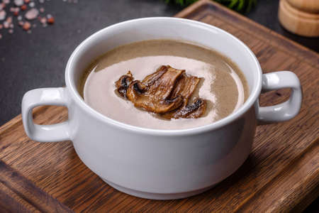 A delicious fresh, thick soup of mushroom puree with breadcrumbs, spices and herbs on a wooden board against a dark concrete background. Vegetarian cuisineの写真素材