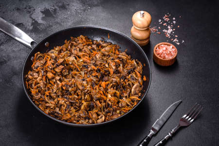 Fried champignons with carrots, onions and spices in a pan against a dark concrete background. Vegetarian cuisineの写真素材