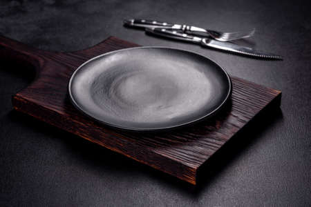 An empty plate with a knife, fork or spoon with a wooden cutting board on a dark concrete background. Preparation of appliances and ingredients for home cookingの写真素材