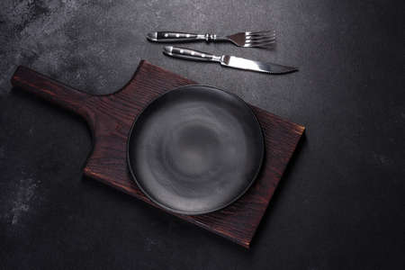 An empty plate with a knife, fork or spoon with a wooden cutting board on a dark concrete background. Preparation of appliances and ingredients for home cookingの写真素材
