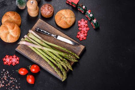 Delicious fresh raw green asparagus stalks on wooden cutting board on festive Christmas table