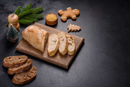 French baguette bread sliced on a wooden cutting board against a dark concrete background. Preparing...