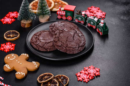 Delicious fresh chocolate biscuits on a dark concrete background with Christmas toys, dried citrus...