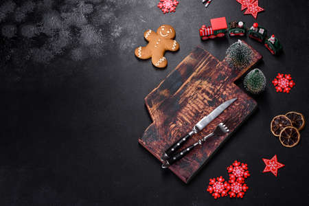 Christmas homemade gingerbread cookies, spices and cutting board on dark background with copy space...
