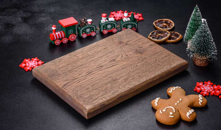 Christmas homemade gingerbread cookies, spices and cutting board on dark background with copy space...