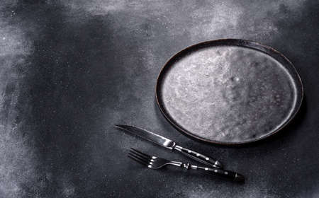 Empty black plates, fork and knife on a gray background. Top view, copy spaceの写真素材