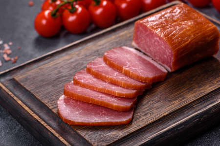 Delicious smoked meat cut with slices on a wooden cutting board against a dark grey concrete backgroundの写真素材