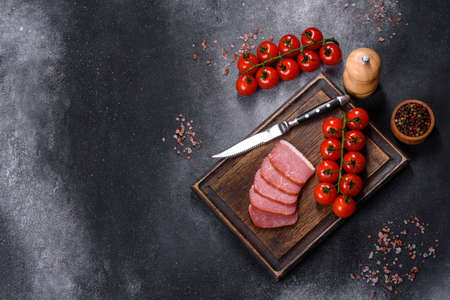 Delicious smoked meat cut with slices on a wooden cutting board against a dark grey concrete backgroundの写真素材