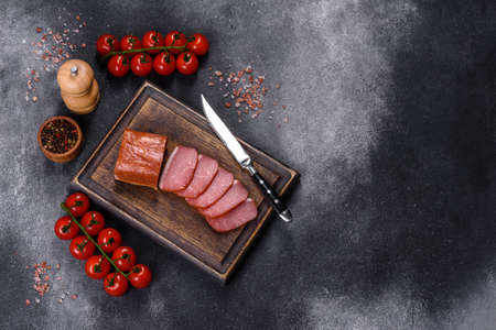 Delicious smoked meat cut with slices on a wooden cutting board against a dark grey concrete backgroundの写真素材